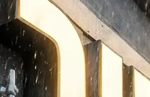 שלט תלת מימד מואר בחיפה עומד בסערה, עם גשם, רוח חזקה וגלי ים המדגישים את חשיבות החומרים העמידים.